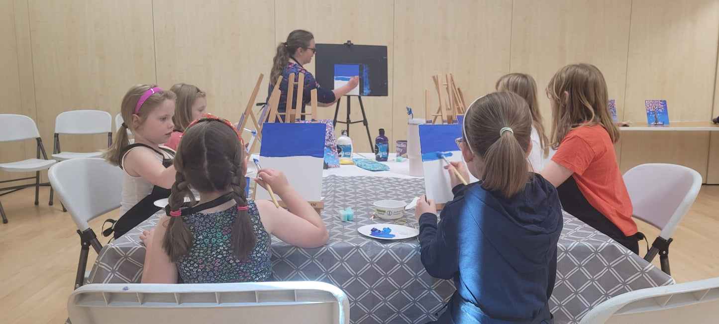 A group of six children sitting around a table painting at easels participating in a Junior Paint and Sip session run by Studio Fifty Art.