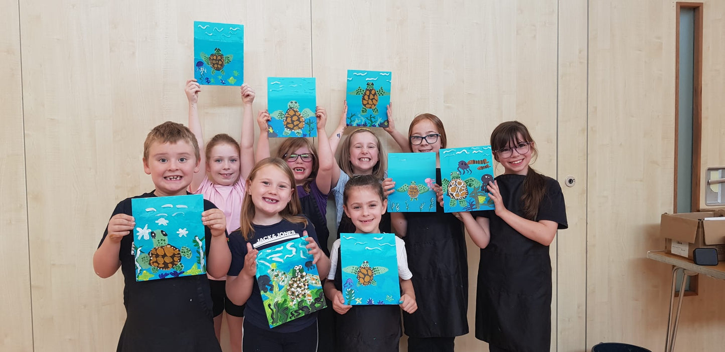 A group of 8 children smiling and holding up their paintings of sea turtles that they'd created during a Junior Paint & Sip session run by Studio Fifty Art