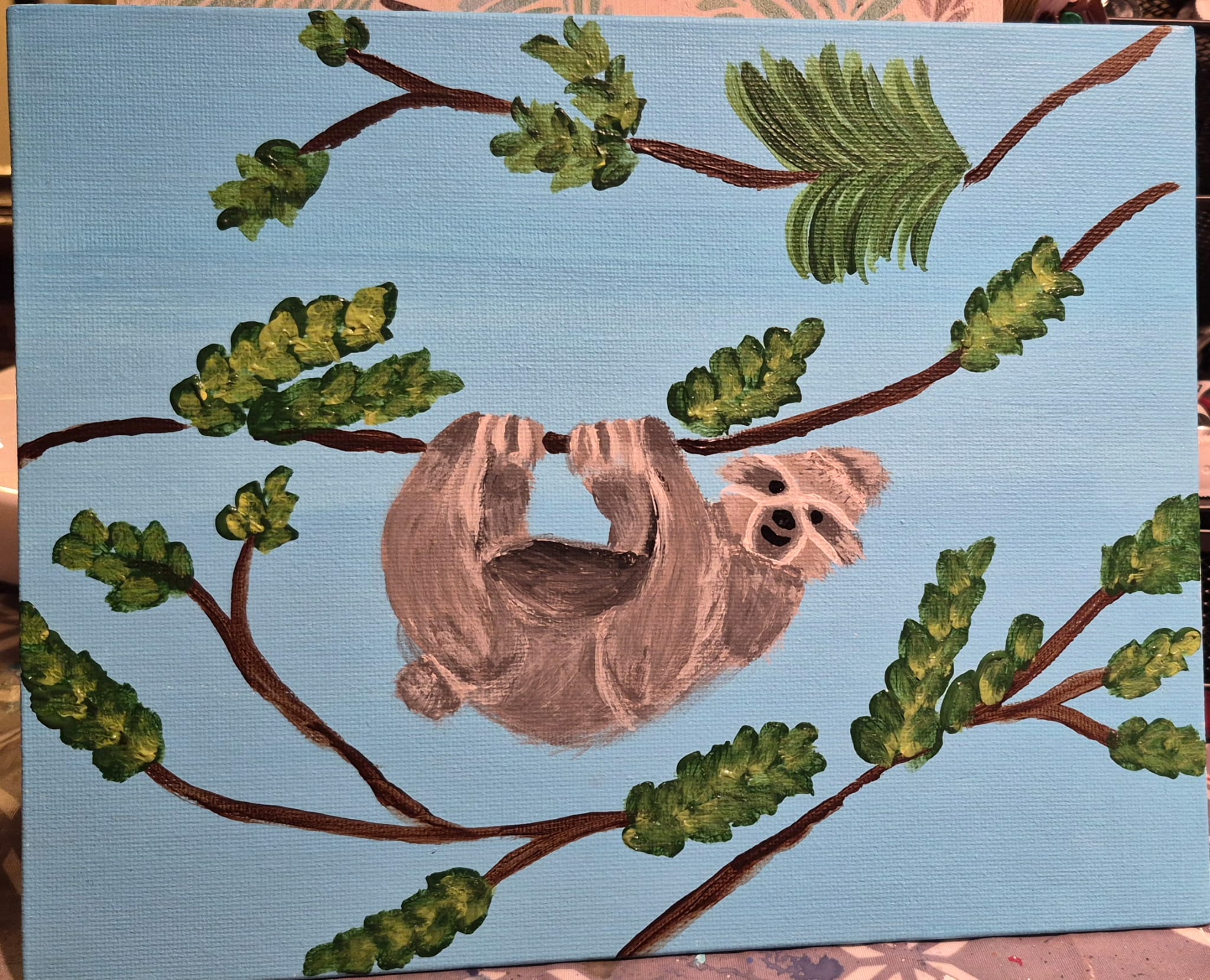 Painting of a sloth hanging from a branch with green leaves on a blue background